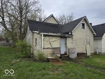 Exterior shot of a neglected house with overgrown foliage and boarded windows in need of renovation at 727 W 25Th St, Indianapolis, IN 46208