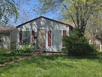 Exterior view of a single-story home with gray siding, red trim, and partially boarded windows at 1138 N Exeter Ave, Indianapolis, IN 46222