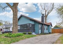Charming blue home featuring a brick chimney, well-manicured lawn, and a paved driveway and mature trees at 3433 Brouse Ave, Indianapolis, IN 46218