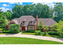 Beautiful brick home featuring a red door, manicured landscaping, and mature trees at 7545 Chablis Cir, Indianapolis, IN 46278
