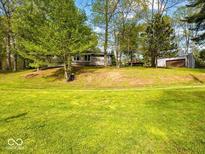 Exterior view of the home with a large grassy front yard and mature trees providing ample shade at 6827 S 500 W, Trafalgar, IN 46181