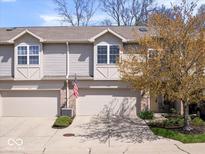 Inviting townhouse featuring an attached garage, mature landscaping, and a charming American flag at 11264 Fonthill Dr, Indianapolis, IN 46236