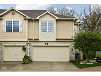 Charming townhome showcasing tan siding and a two-car garage, complemented by a well-manicured lawn and vibrant flower display at 1032 Grovewood Dr # 0, Beech Grove, IN 46107