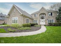 Beautiful brick home with manicured lawn and landscaping leading to an arched entry at 3837 Penzance Pl, Carmel, IN 46032
