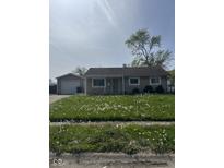 Quaint single-story home with a detached garage and dandelion filled front lawn at 2448 Winfield Ave, Indianapolis, IN 46222