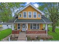 Charming yellow two-story home featuring a welcoming front porch with brick accents and a classic white picket fence at 25 N Wayburn St, Indianapolis, IN 46229