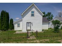 Charming white home featuring black roof, wrought iron fence, manicured lawn, and bright blue sky at 2402 N B St, Elwood, IN 46036
