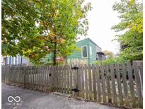 View of the home with green siding and a wooden fence in the front yard and mature trees at 949 Harrison St, Indianapolis, IN 46202