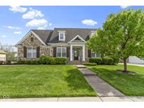 Charming stone home featuring a manicured lawn, lush landscaping, and inviting front entrance at 3965 Andretti Dr, Zionsville, IN 46077