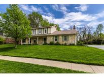 Charming two-story home featuring a stone facade, covered porch, well-manicured lawn, and lush landscaping at 7423 Scarborough Blvd E Dr, Indianapolis, IN 46256