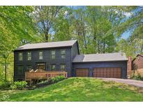 Two-story home with wood siding, attached garage, and a wooden deck surrounded by lush trees and greenery at 10455 Courageous Dr, Indianapolis, IN 46236