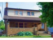Charming two-story home featuring a brick facade and inviting front porch with well-maintained landscaping at 6051 Lowell Ave, Indianapolis, IN 46219