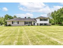 Charming two-story home with light brick, black shutters, an expansive lawn, and lush landscaping at 7250 Hoover Rd, Indianapolis, IN 46260