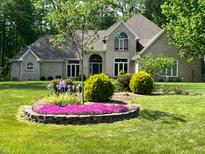 Charming brick home featuring a lush, landscaped front yard with colorful flower beds and mature trees at 3948 S Woodfield Dr, New Palestine, IN 46163
