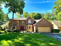 Inviting two-story brick home boasts mature trees, manicured lawn, and red front door at 7621 Forest Dr, Fishers, IN 46038