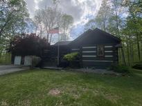 Beautiful log-cabin home featuring a covered porch with an American flag waving in a serene wooded setting at 7916 N Lasalle Rd, Morgantown, IN 46160