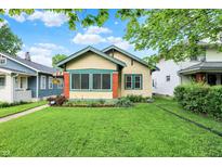 Charming yellow home with green trim, brick accents, a well-manicured lawn and beautiful landscaping at 844 N Emerson Ave, Indianapolis, IN 46219