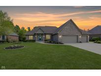 Charming brick home featuring an attached three-car garage, well-manicured lawn, and colorful garden beds at 1297 Morningside Dr, Greenfield, IN 46140