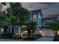 Charming two-story home featuring a covered front porch, attached garage, and well-manicured lawn at dusk at 7218 Antiquity Dr, Carmel, IN 46033