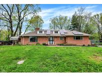 Charming brick home featuring solar panels, a well-maintained lawn, and mature trees, all under a bright blue sky at 3975 Denwood Dr, Indianapolis, IN 46226