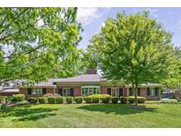 Charming red brick home features a landscaped lawn, mature trees, and classic black shutters at 7843 Windcombe Blvd, Indianapolis, IN 46240