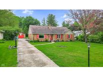 Charming brick home with red shutters, a well-manicured lawn, and a concrete walkway and drive at 1107 N Hartman Dr, Indianapolis, IN 46219
