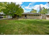 Charming single-story home with stone facade, a large tree, green lawn, and an American flag at 1701 Lincoln Rd, Speedway, IN 46224