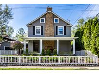 Charming two-story home featuring gray siding, brick chimney, a front porch, and a neatly manicured yard at 413 E 40Th St, Indianapolis, IN 46205