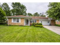 Charming brick home featuring a well-manicured lawn, flower beds, and attached two-car garage with basketball hoop at 8103 Rumford Rd, Indianapolis, IN 46219