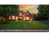 Charming brick home with a manicured lawn and beautiful landscaping, illuminated by warm exterior lighting at 11245 Old Stone Dr, Indianapolis, IN 46236