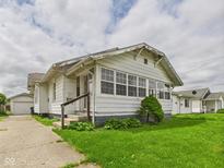 Quaint single-story home with weathered white siding, green lawn, and a detached garage at 717 E 27Th St, Anderson, IN 46016