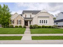 Charming two-story home with stone and brick, complemented by a lush green lawn and inviting walkway at 14003 Grannan Ln, Carmel, IN 46074