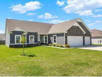 Charming single-story home with gray siding, stone accents, a well-manicured lawn, and a 3 car garage at 49 Manchester Dr, Trafalgar, IN 46181