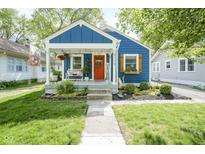 Charming blue home featuring a cozy front porch and a vibrant orange door, complemented by lush landscaping at 5119 Ralston Ave, Indianapolis, IN 46205