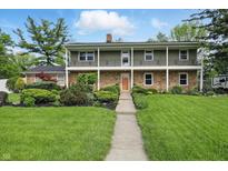 Charming two-story brick home with lush landscaping and a welcoming front porch at 6825 Farmleigh Dr, Indianapolis, IN 46220