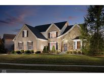 Elegant brick and stone home featuring a manicured lawn, lush landscaping, and a welcoming arched entryway at dusk at 14707 Thor Run Dr, Fishers, IN 46040