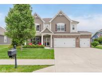 Charming two-story home featuring a brick facade, three-car garage, manicured lawn, and lush landscaping at 15143 Gallop Ln, Fishers, IN 46040