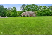 Expansive front yard featuring a charming brick home surrounded by lush greenery and mature trees at 2508 Indian Creek Rd, Trafalgar, IN 46181