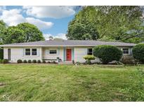 Charming one-story home with a well-manicured lawn, vibrant landscaping, and a striking red front door at 7277 N College Ave, Indianapolis, IN 46240