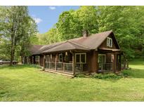Charming cabin-style home featuring a covered porch, wood siding, and lush green lawn surrounded by trees at 7730 Bear Creek Rd, Morgantown, IN 46160