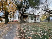 Quaint, two-story home featuring a covered porch and mature trees, set amidst a colorful autumn landscape at 8345 N State Road 109, Wilkinson, IN 46186