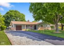 Charming single-story home boasts an attached garage and is enhanced by a lush front yard with mature trees at 8120 E 11Th St, Indianapolis, IN 46219