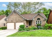 Charming brick home featuring a two-car garage, well-manicured lawn, and colorful flower beds at 3348 Fox Orchard Cir, Indianapolis, IN 46214