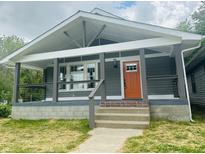 Charming home featuring a covered front porch, gray siding, an orange front door, and manicured lawn at 1718 Thaddeus St, Indianapolis, IN 46203