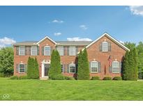 Beautiful brick home with manicured lawn, symmetrical evergreens and classic architectural details, under a clear blue sky at 3267 Cimmaron Ash Ct, Zionsville, IN 46077