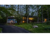 Serene wooded property showcasing an architecturally striking stone home with illuminated interiors for a warm and inviting feel at 12469 Springmill Rd, Carmel, IN 46032
