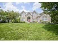 Stunning brick home featuring a large front yard, red door, and mature trees at 13244 Snow Owl Dr, Carmel, IN 46033