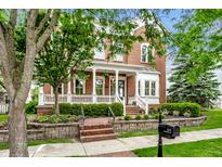 Inviting red brick home featuring a charming front porch, well-manicured lawn, and professional landscaping at 2037 Stanhope St, Carmel, IN 46032