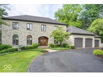 Stunning stone-clad home featuring an arched entry, meticulously manicured landscaping, and an attached three-car garage at 11715 Landings Dr, Indianapolis, IN 46256