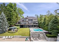 Stunning lakefront home featuring a pool, stone terrace, and lush landscaping with mature trees at 11715 Landings Dr, Indianapolis, IN 46256